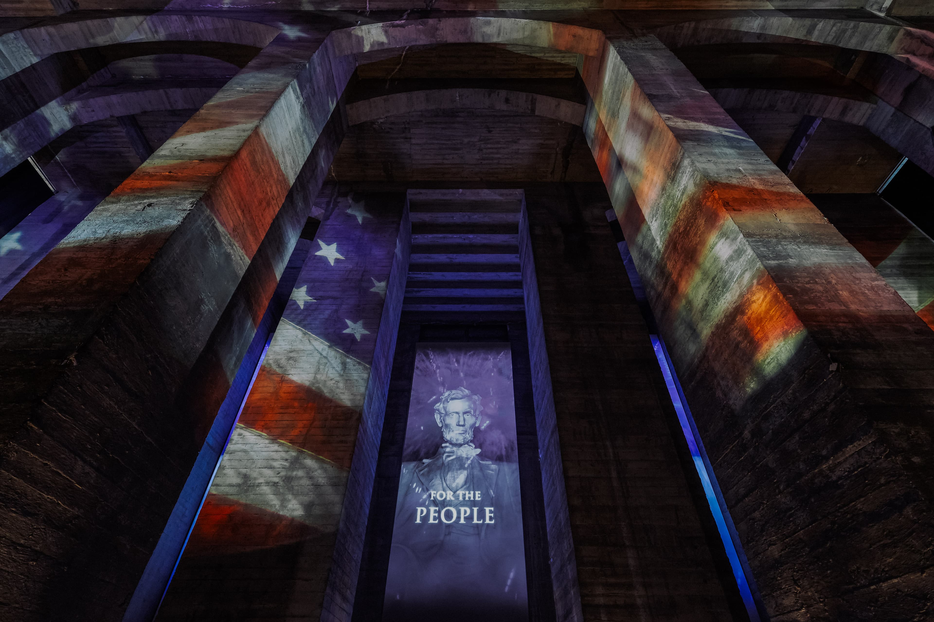 A view of the Lincoln Undercroft looking up. The entire area is lit up with a projection of a waving American flag.