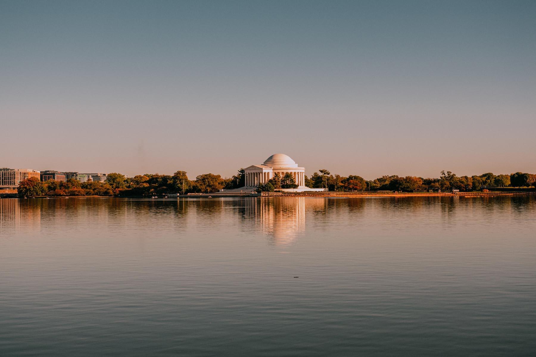 Distant view of the Thomas Jefferson Memorial reflected in the calm waters of the Tidal Basin under a clear sky.