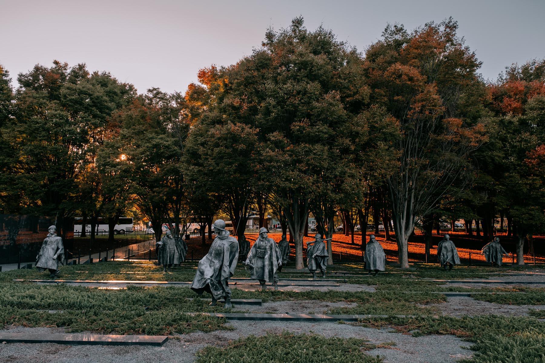 Panoramic view of the Korean War Veterans Memorial statues, with trees and the engraved reflective wall in the background.