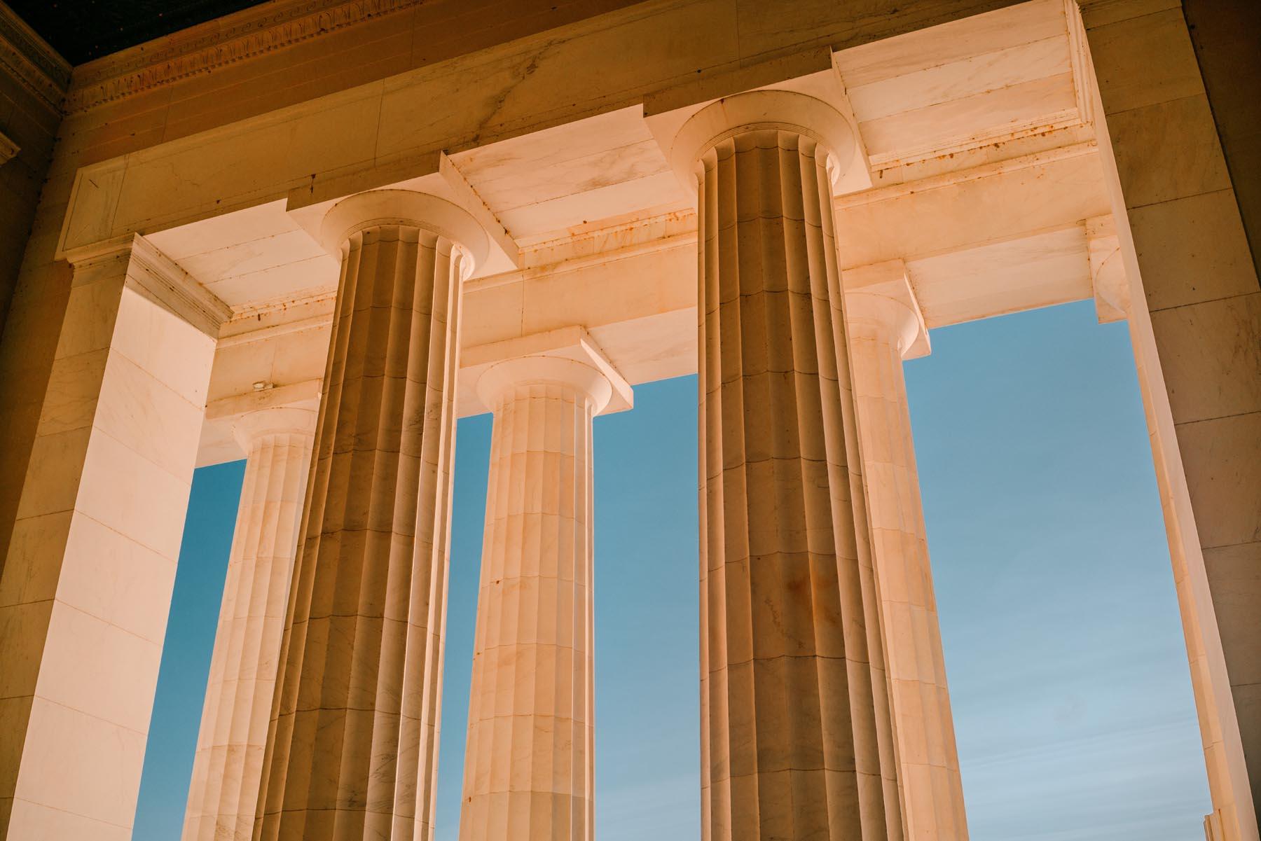 Low-angle shot of the Lincoln Memorial columns, highlighting the intricate architectural details with a bright blue sky in the background.