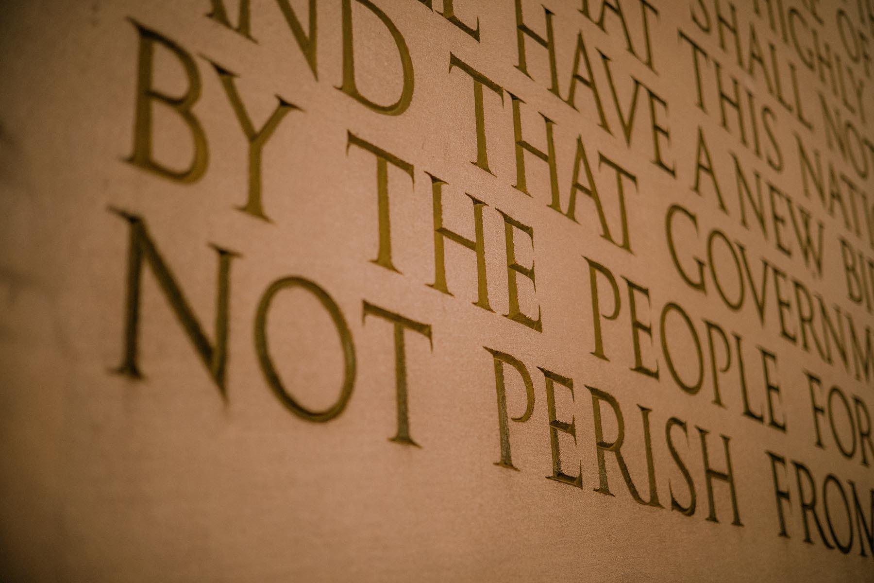 A detailed view of a section of the Gettysburg Address inscription at the Lincoln Memorial, focusing on the words "by the people" and "not perish."
