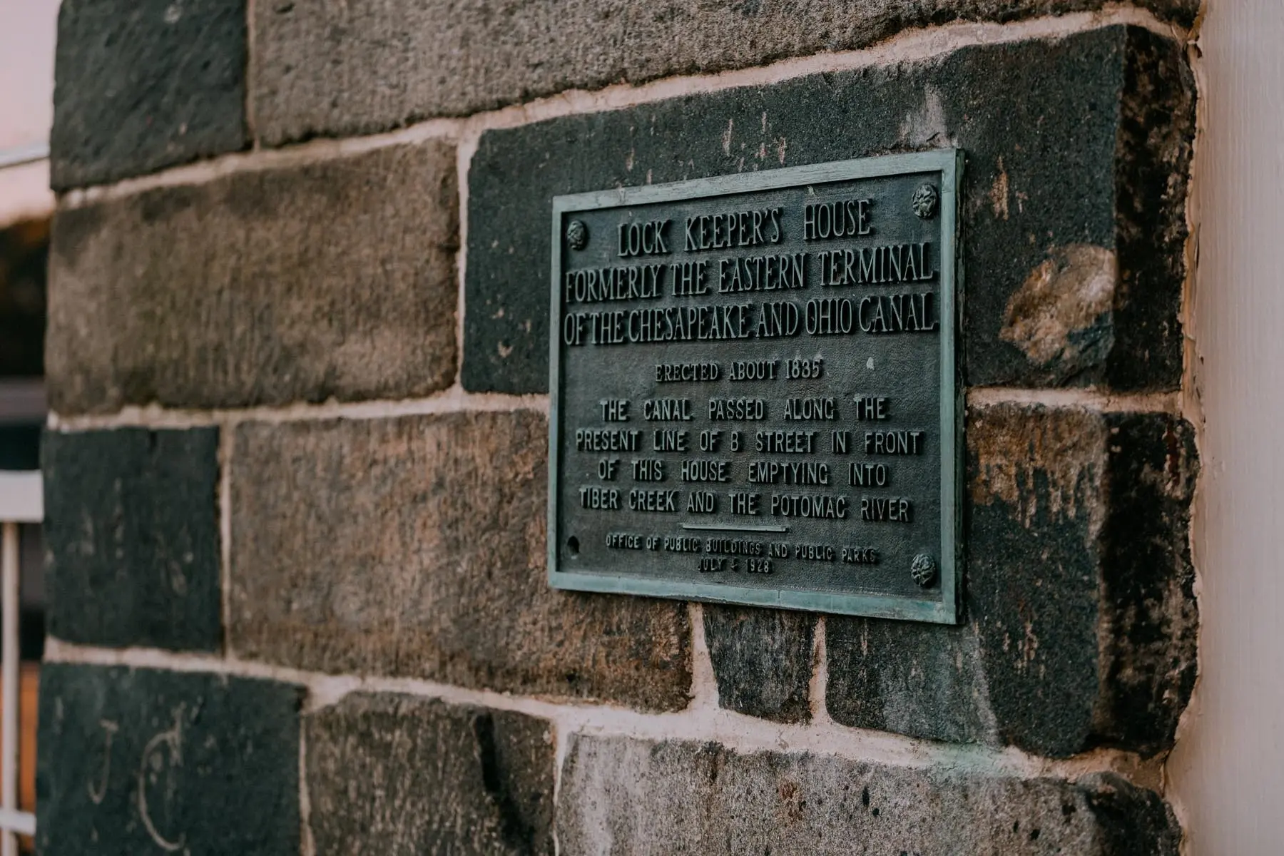 Close-up of a plaque on the exterior stone wall of the Lockkeeper's House. The text describes its history as the eastern terminal of the Chesapeake and Ohio Canal, constructed around 1835.