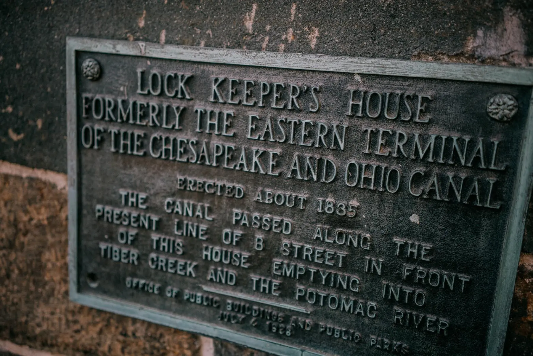 Tight close-up of the historical plaque on the Lockkeeper's House, showing the embossed details about the building's role and construction date.