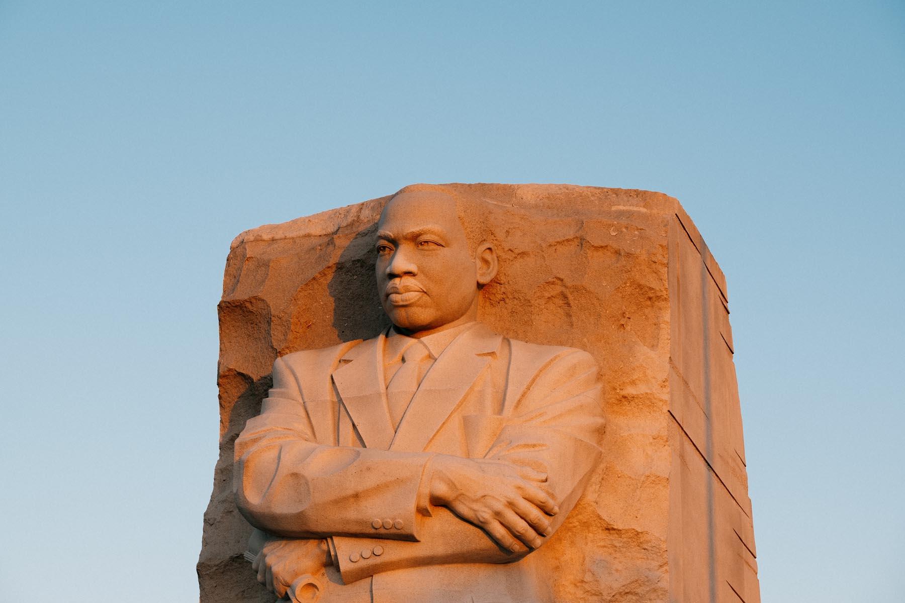 zoomed-in view of the Martin Luther King Jr. statue, focused on his face and upper body, with the warm tones of sunset reflecting off the stone.