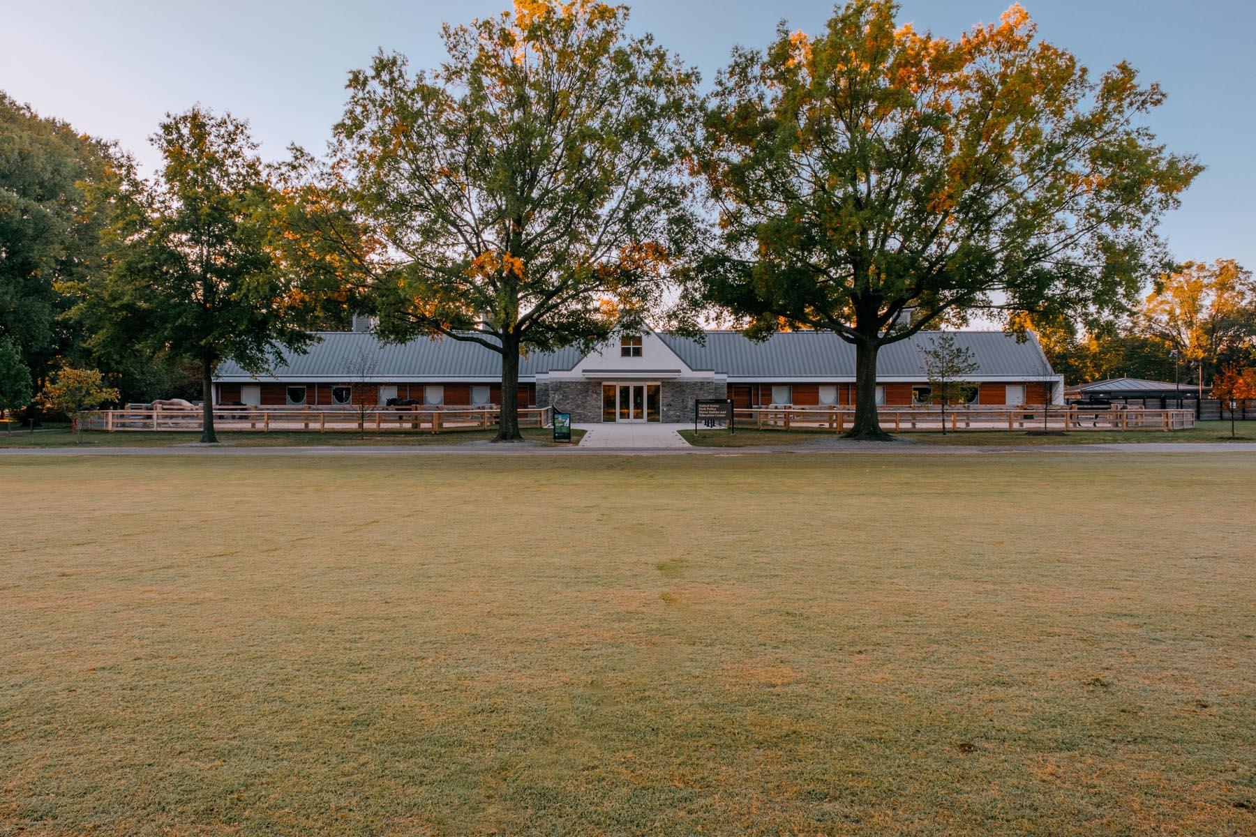 A wide view of the U.S. Park Police Horse Stables and Education Center, with the stable building framed by trees and a grassy lawn in the foreground.