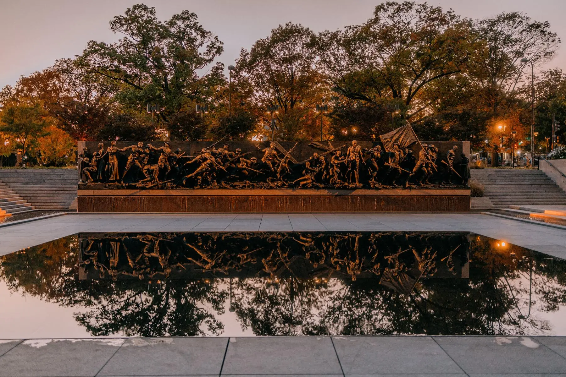 Symmetrical view of the WWI memorial with the bronze relief sculptures mirrored in the calm waters of the reflecting pool, framed by the autumnal setting of Washington, DC.