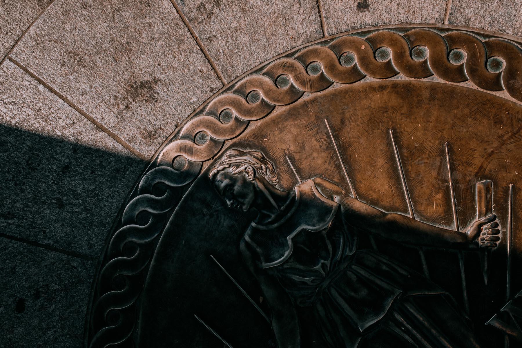 Detailed shot of a bronze relief depicting a female figure, part of the WWII Memorial, framed by a patterned border and illuminated by angled light.