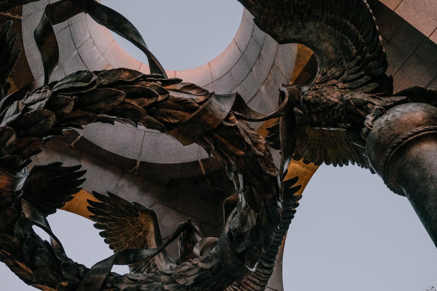 Close-up of the laurel wreath held by bronze eagles in the Atlantic Pavilion at the WWII Memorial, with a clear evening sky visible through the architectural circle.
